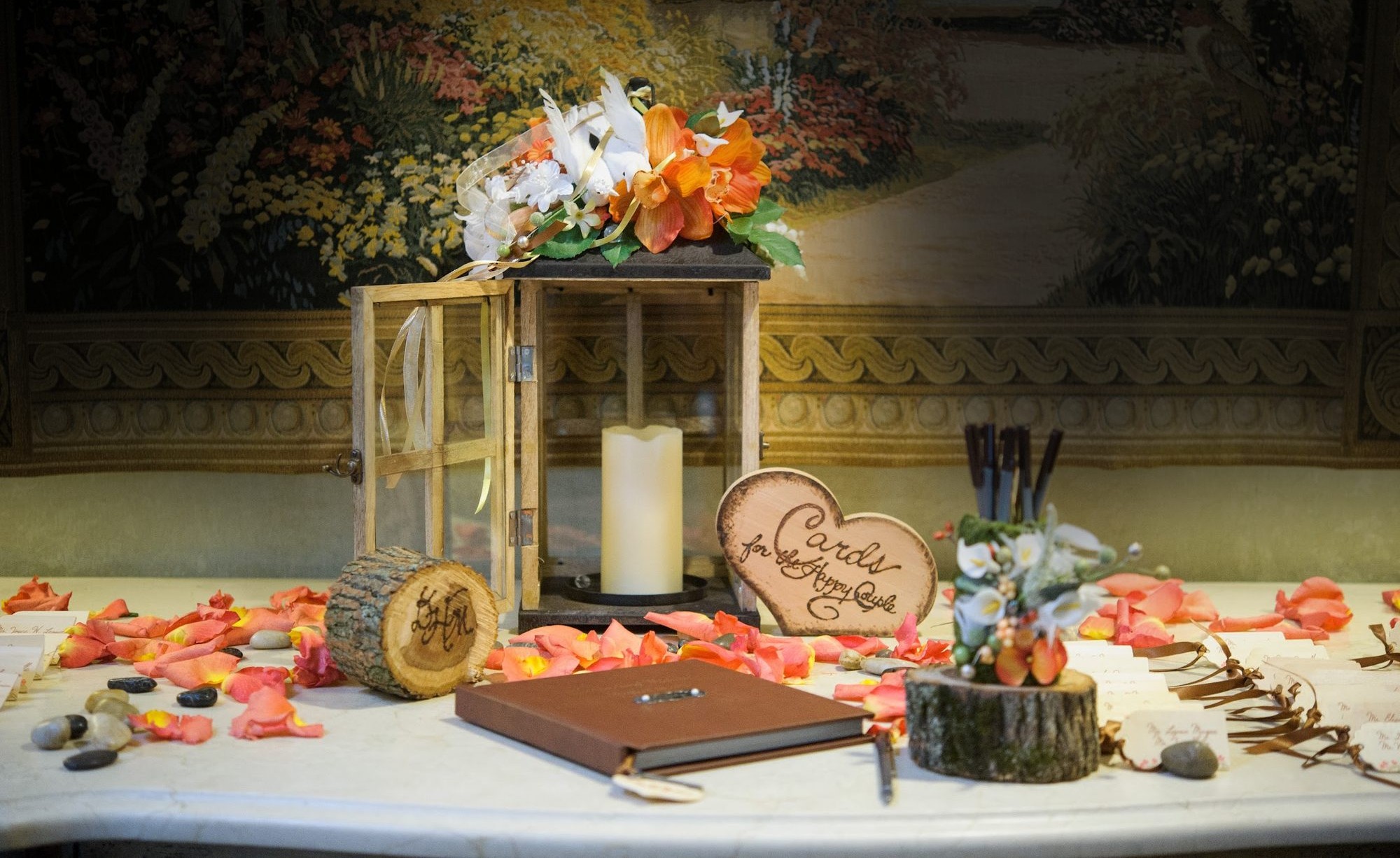 The guest-book table &mdash; lantern, wood-burned hearts, and petals glowing against the darkened tapestry