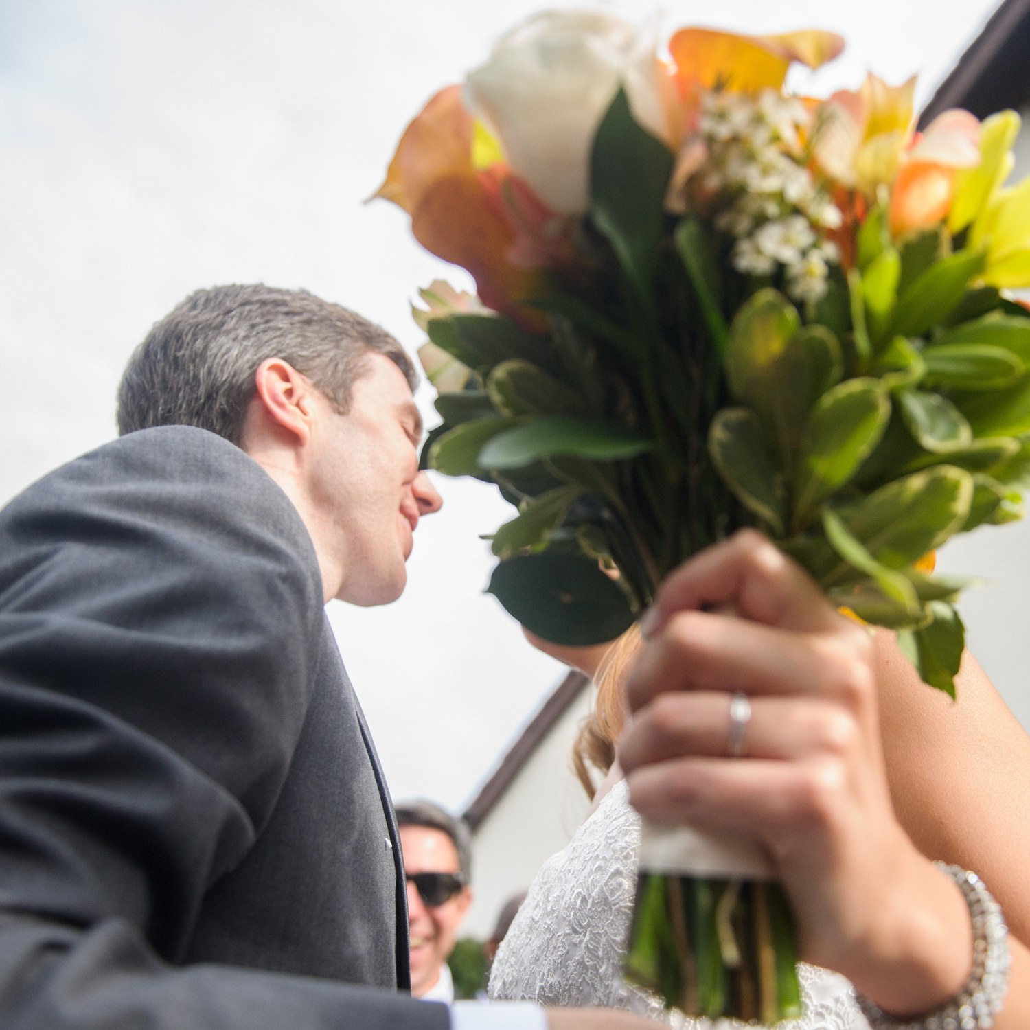 A stolen kiss behind the bouquet &mdash; her ring hand wrapped around the stems