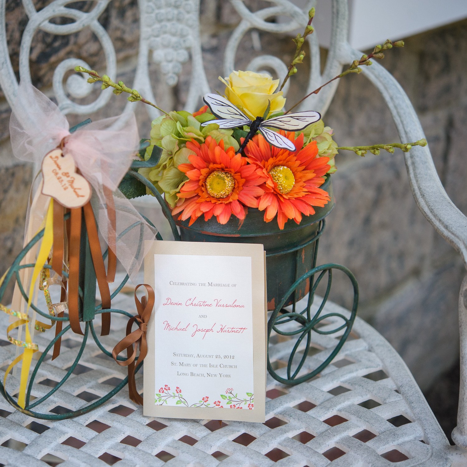 The wedding program on an iron chair beside a dragonfly flower-cart arrangement